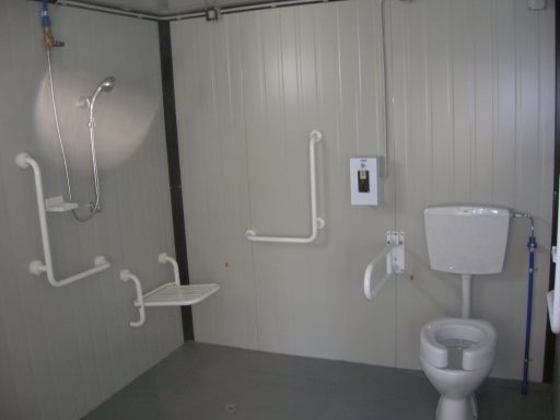 Salle de bain accessible avec douche, toilettes et barres d'appui.