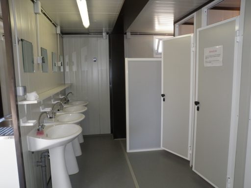 Sanitaires avec lavabos et cabines de toilettes, murs clairs et lumière fluorescente.